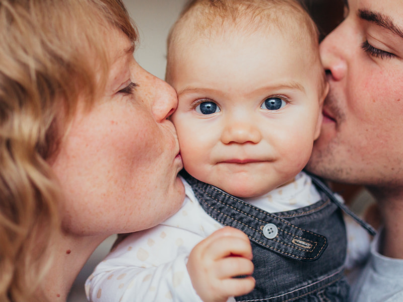 Mãe e pai a beijar o seu bebé em cada bochecha simultaneamente